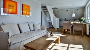 En moderne stue med en sofa, et træsofabord og en trappe, der fører op til et køkken.