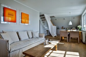 Ein modernes Wohnzimmer mit einer Couch, einem Holztisch und einer Treppe, die in eine Küche führt.