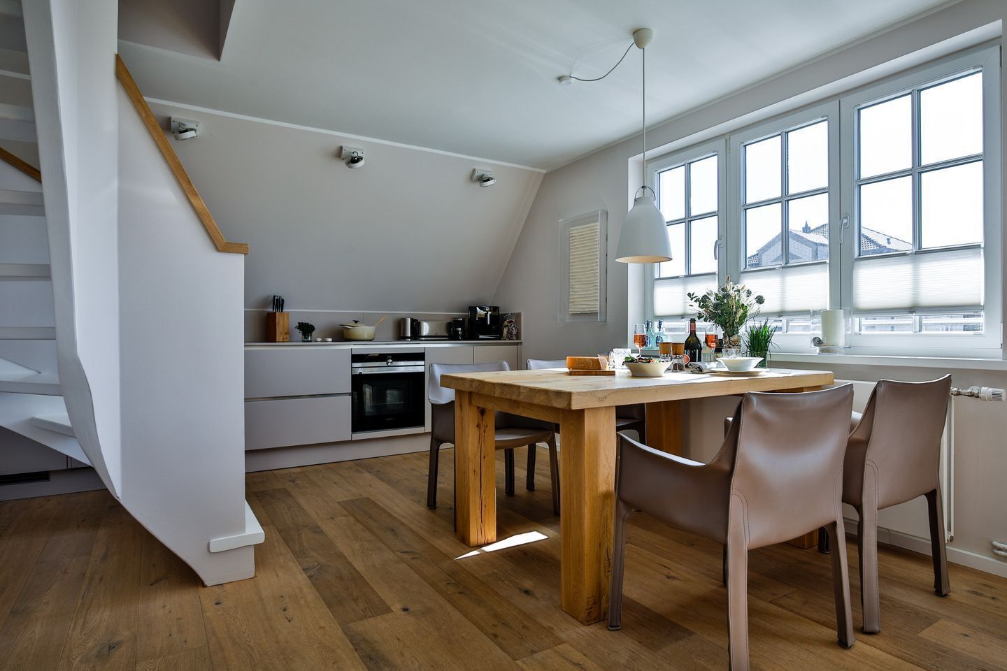 Een moderne keuken met een eethoek, houten vloeren en uitzicht door grote ramen.