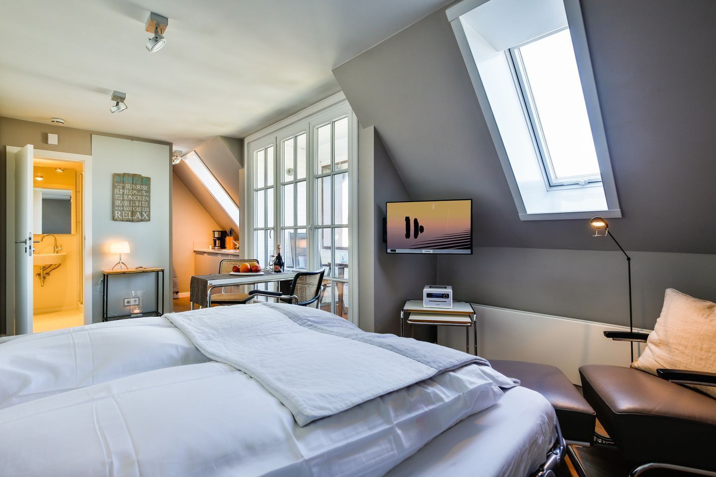 Una habitación de hotel con una cama grande, un escritorio con una computadora, un televisor y un tragaluz.