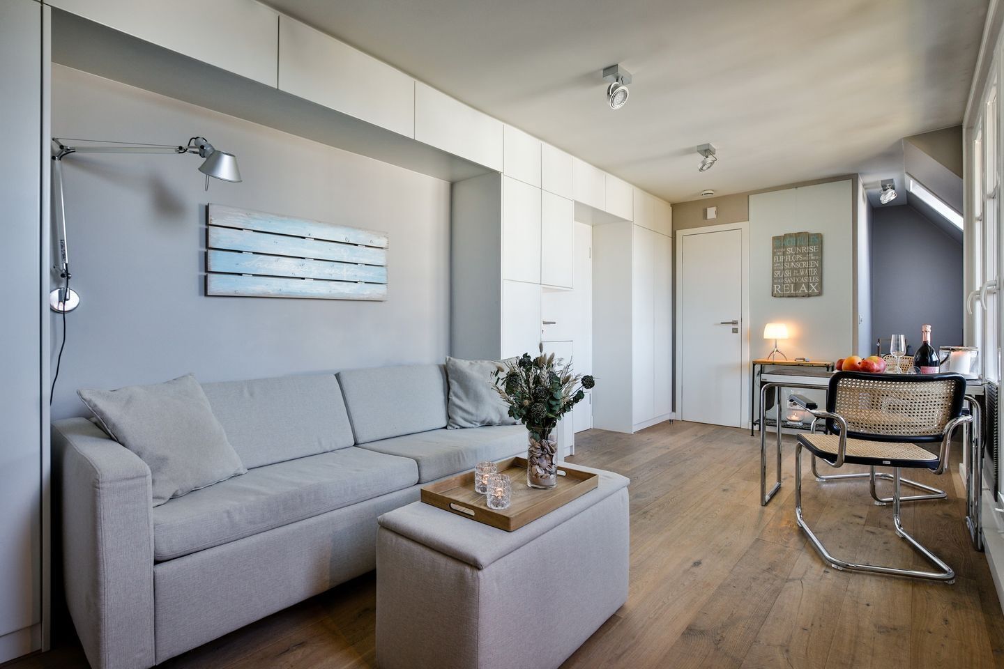 A modern living room with a grey sofa, a wooden coffee table, and a dining area with a metal chair and table.