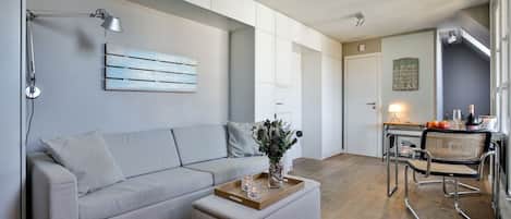 A modern living room with a grey sofa, a wooden coffee table, and a dining area with a metal chair and table.