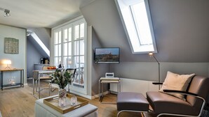 Una sala de estar moderna con techo estilo loft, un comedor con mesa y sillas, un sofá, un televisor y un ventanal con vistas.