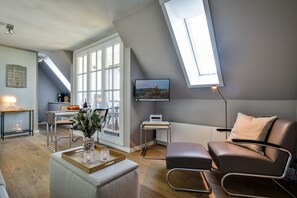 Ein modernes Wohnzimmer mit Mansardedecke, einem Essbereich mit Tisch und Stühlen, einer Couch, einem Fernseher und einem Fenster mit Aussicht.