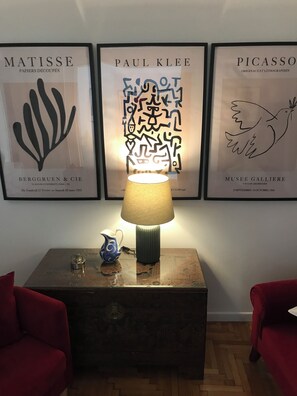A room with a wooden side table, a lamp, and three framed artworks on the wall. - Elegant Pangrati Apartment Near Metro & Museums 
Entire apartment Up to 4 people (Athina)
