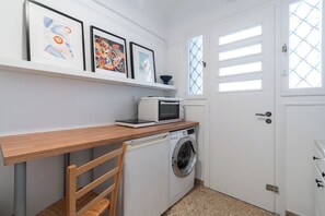 A compact laundry room with a washing machine, a microwave, and a shelf with framed artwork. - Elegant Pangrati Apartment Near Metro & Museums 
Entire apartment Up to 4 people (Athina)