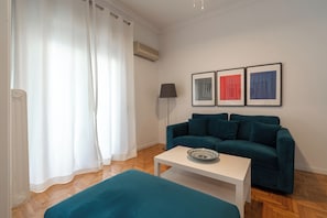 A modern living room with a teal sofa, a white coffee table, and a floor lamp. There are three framed artworks on the wall. - Elegant Pangrati Apartment Near Metro & Museums 
Entire apartment Up to 4 people (Athina)