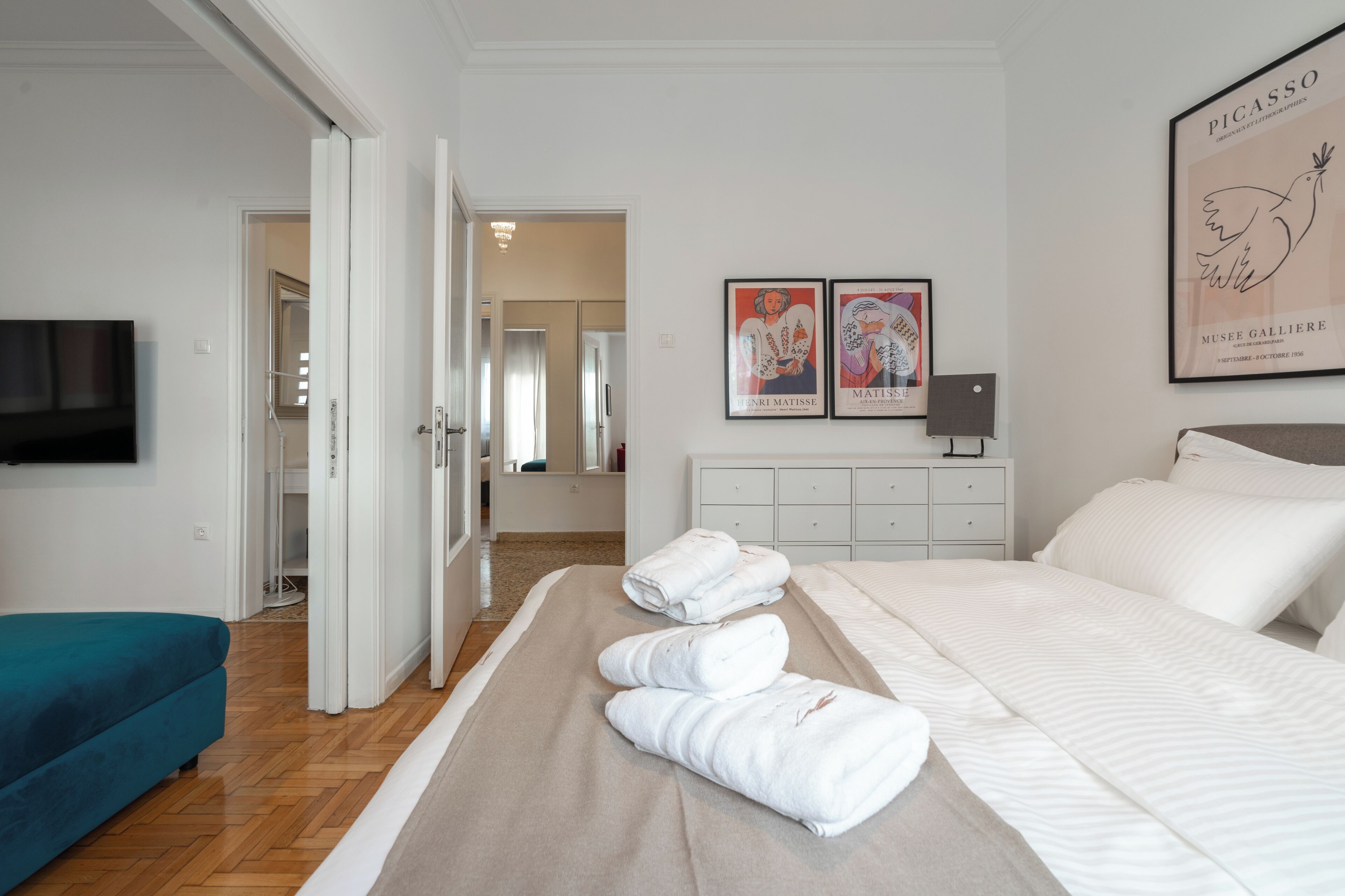 Une chambre d’hôtel avec un lit, un canapé bleu, une télévision, une commode et deux œuvres d’art encadrées accrochées au mur.