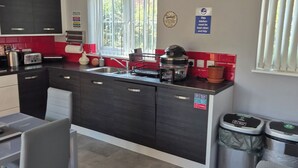 A modern kitchen with a central island, a dining area with a table and chairs, and a view of the outdoors through a window. - Charming Guest Room in West Midlands with Modern Amenities (West Midlands)