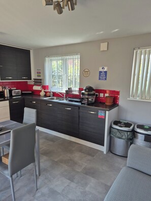 A modern kitchen with a central island, a dining area with a table and chairs, and a view of the outdoors through a window. - Charming Guest Room in West Midlands with Modern Amenities (West Midlands)