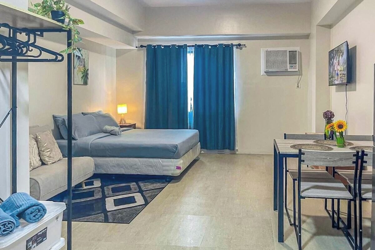 Ein kompakter Wohnraum mit Bett, Sofa, Esstisch mit Stühlen und an der Wand montiertem Fernseher.