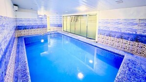 Una piscina interior con agua cristalina, paredes enlosadas y una puerta de vidrio que da a otra habitación.