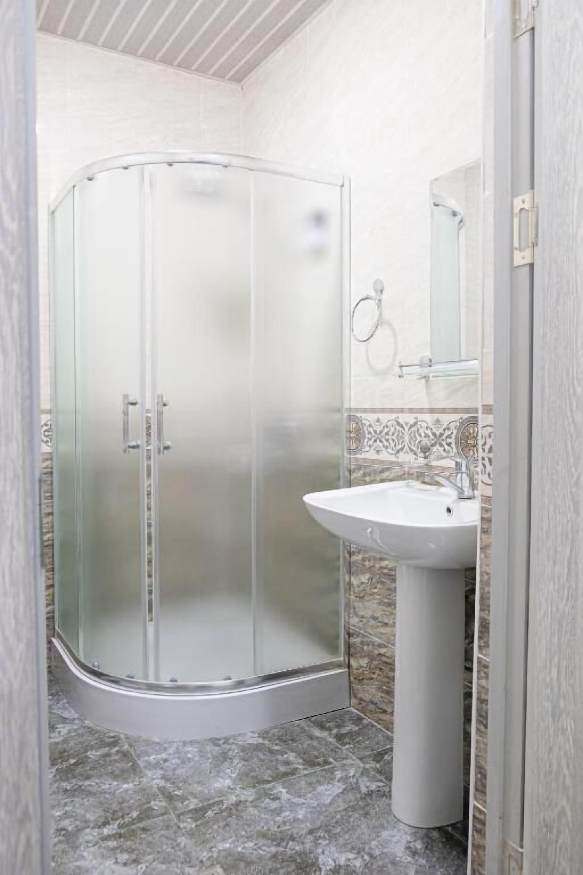 Un baño con ducha de vidrio, lavamanos pedestal y salpicadero de azulejos.