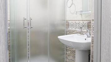 Un baño con ducha de vidrio, lavamanos pedestal y salpicadero de azulejos.