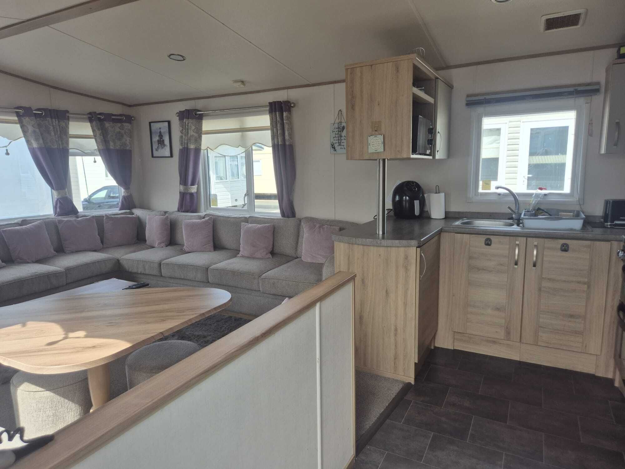 A compact living space with a sofa, a coffee table, a kitchenette, and a window with curtains.