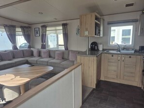 A compact living space with a sofa, a coffee table, a kitchenette, and a window with curtains.