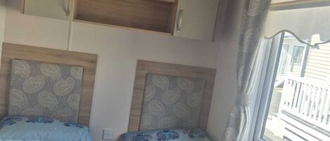 A bedroom with two beds, each with a cartoon character print, a wooden shelf above, and a window with curtains.