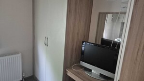 Ein Zimmer mit einem weißen Kleiderschrank, einem Holzschrank, einem Fernseher auf einem Schrank und einer Heizung.