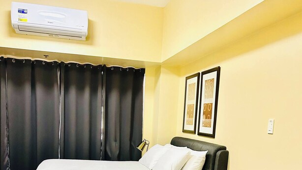 Een kamer met een bed, een grijze bank, een zwart gordijn en een airconditioning.