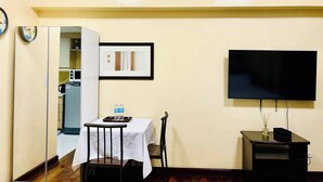 Een ruimtelijk ingerichte leefruimte met een eethoek, een kitchenette, een flatscreen-televisie en een klein tafeltje met dienblad.