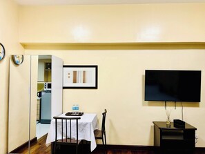 A compact living space with a dining area, a kitchenette, a flat-screen TV, and a small table with a tray. - Staycation away from home (Makati City)