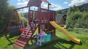 Une structure de jeux en bois comprenant un toboggan, un filet d’escalade et une balançoire.