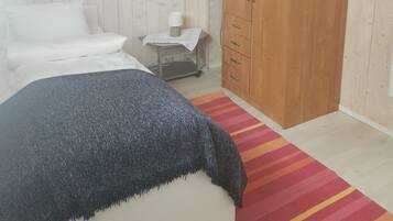 Ein Schlafzimmer mit einem Bett, einem Kleiderschrank, einem Nachttisch mit Lampe und einem Streifen Teppich.