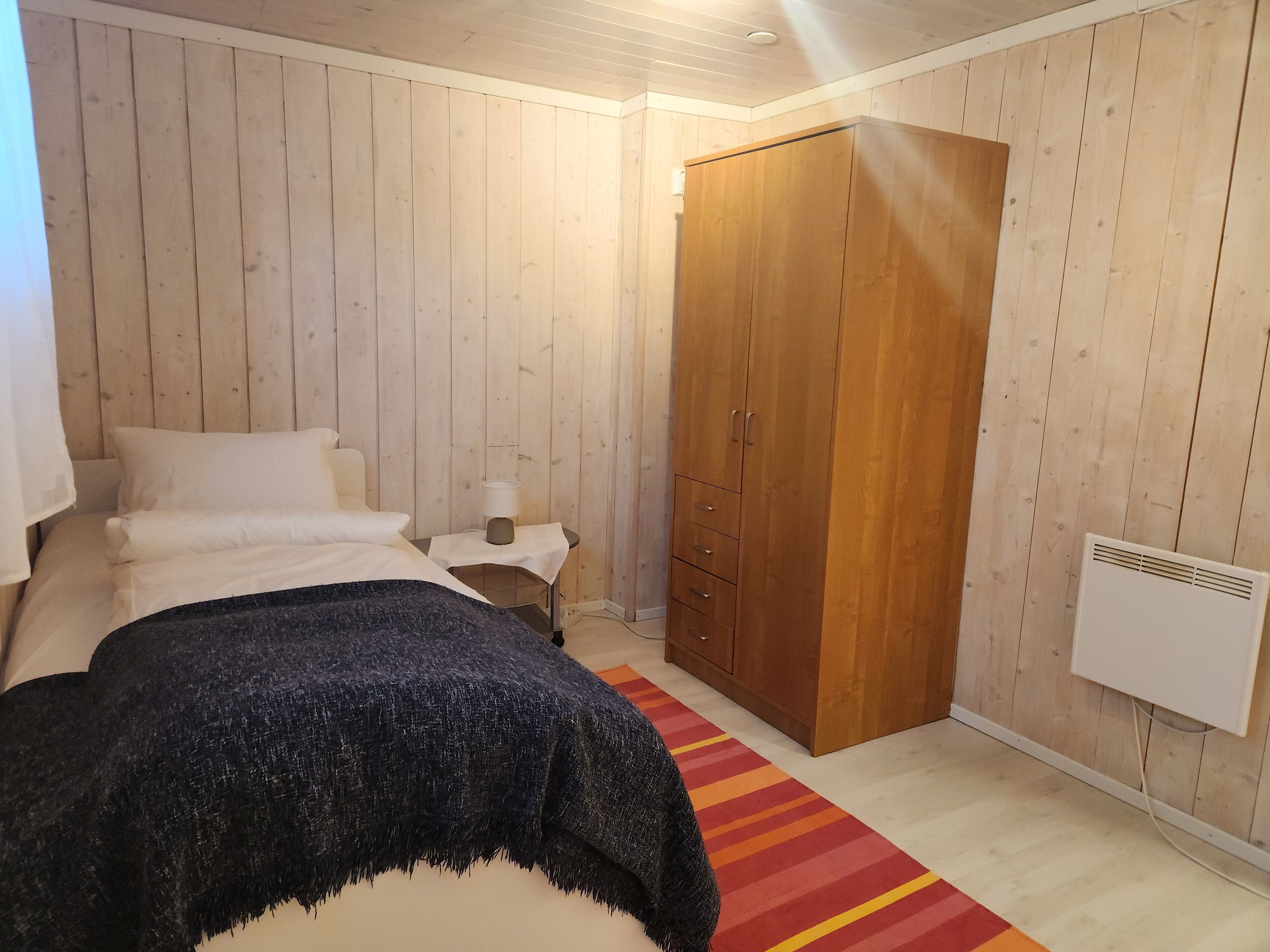 Een slaapkamer met een bed, nachtkastje, kast en radiator.
