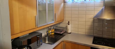 A kitchen with wooden cabinets, a stainless steel sink, a microwave, a kettle, and a stove.