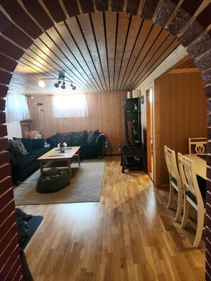 A cozy living room with a wooden ceiling, a sofa, a coffee table, and a dining area with chairs.