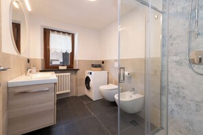 Un baño moderno con cabina de ducha de vidrio, lavadora integrada, bidé y tocador con espejo.