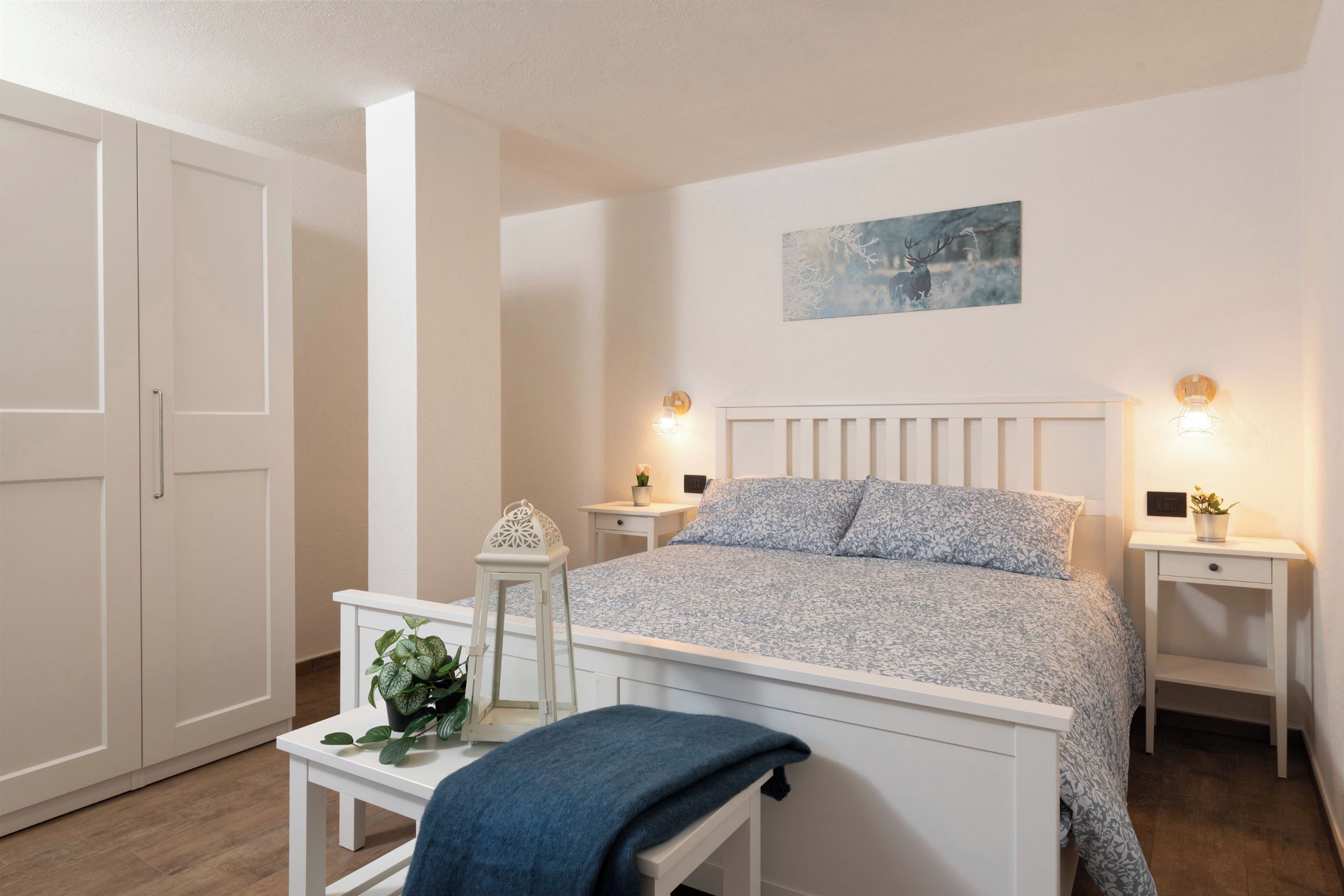 Une chambre à coucher comprenant un lit, des tables de chevet, une commode, un banc et un luminaire fixé au mur.