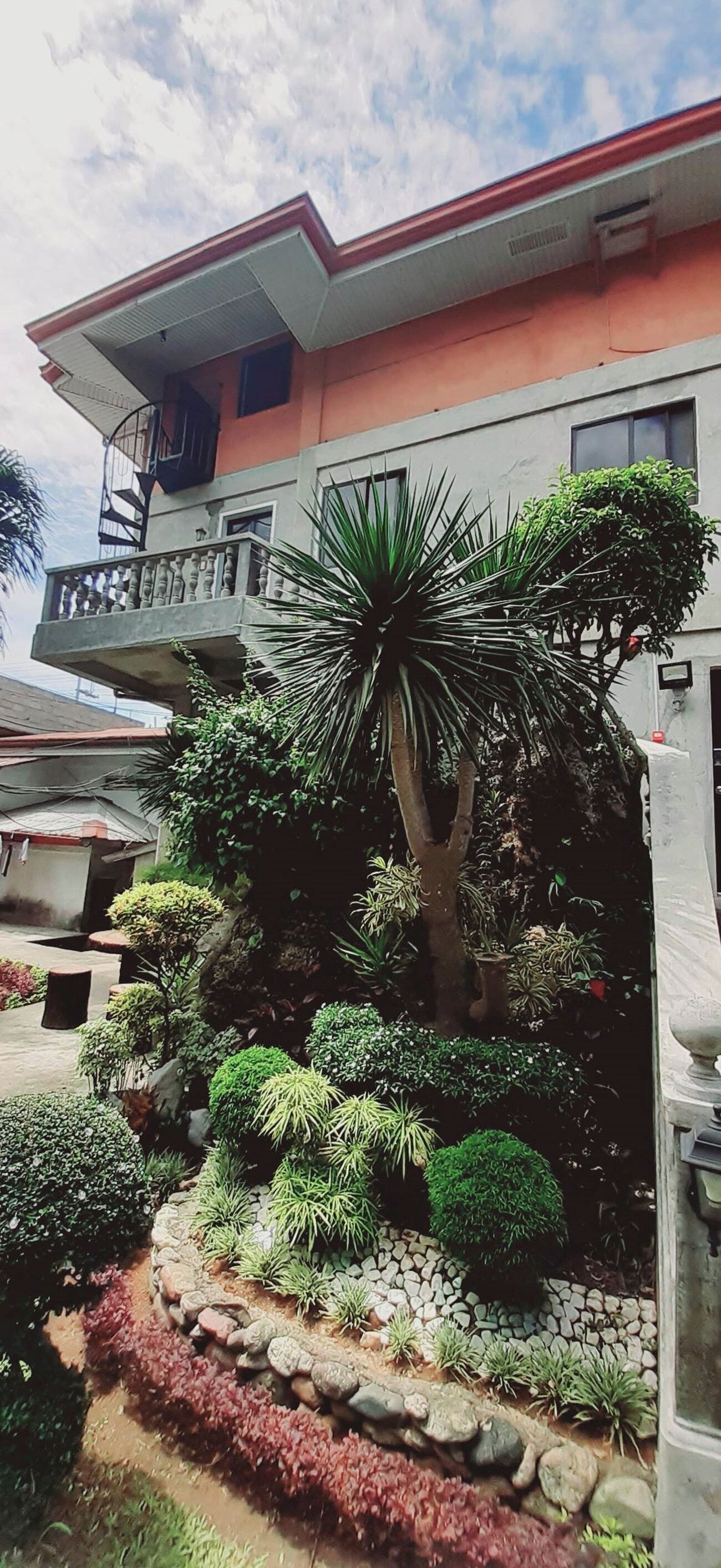 Un edificio con balcón, rodeado de plantas y un sendero de piedra.