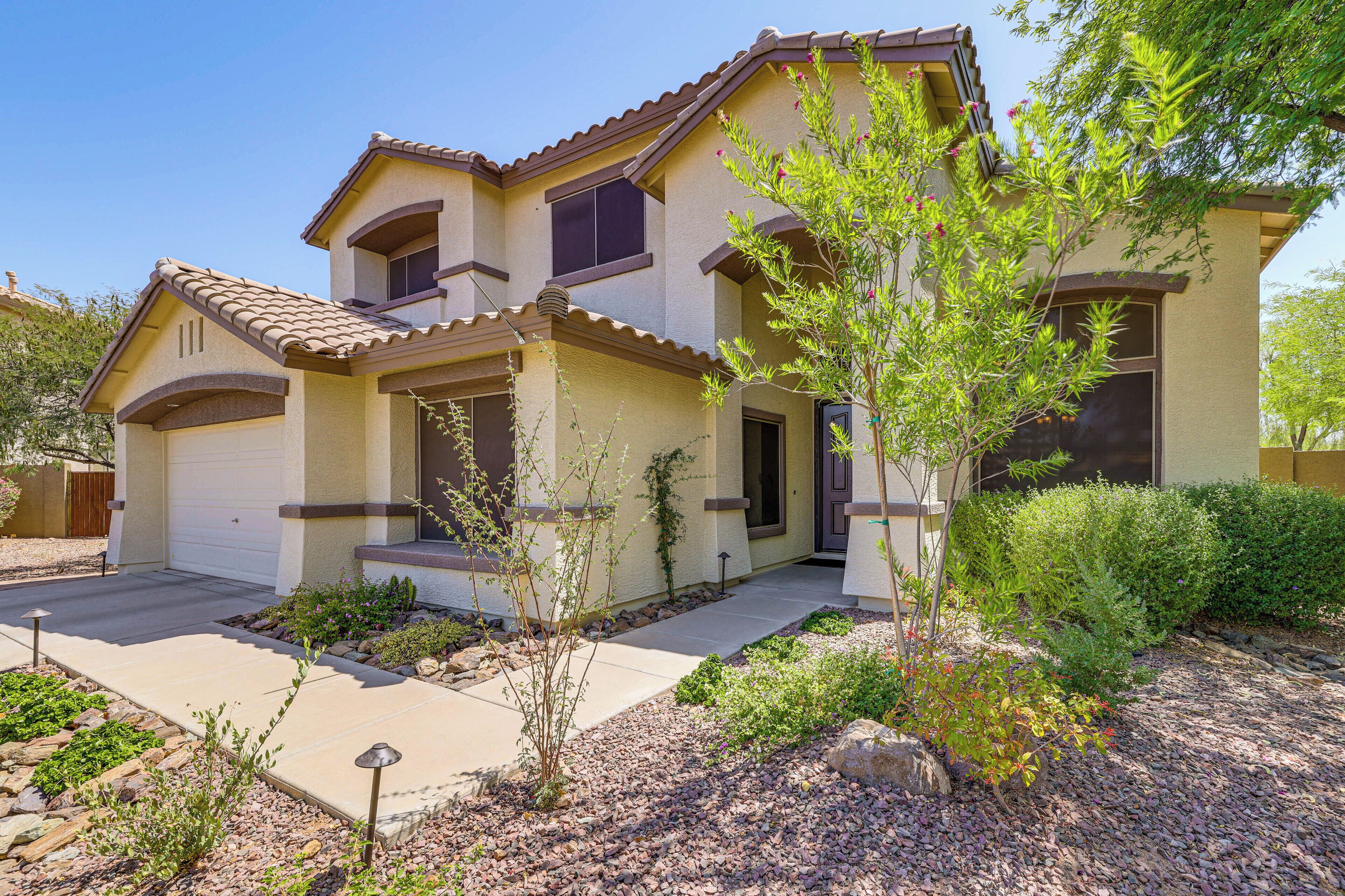 A two-story house with a tiled roof, a front porch, and a landscaped garden with various plants and a small tree.