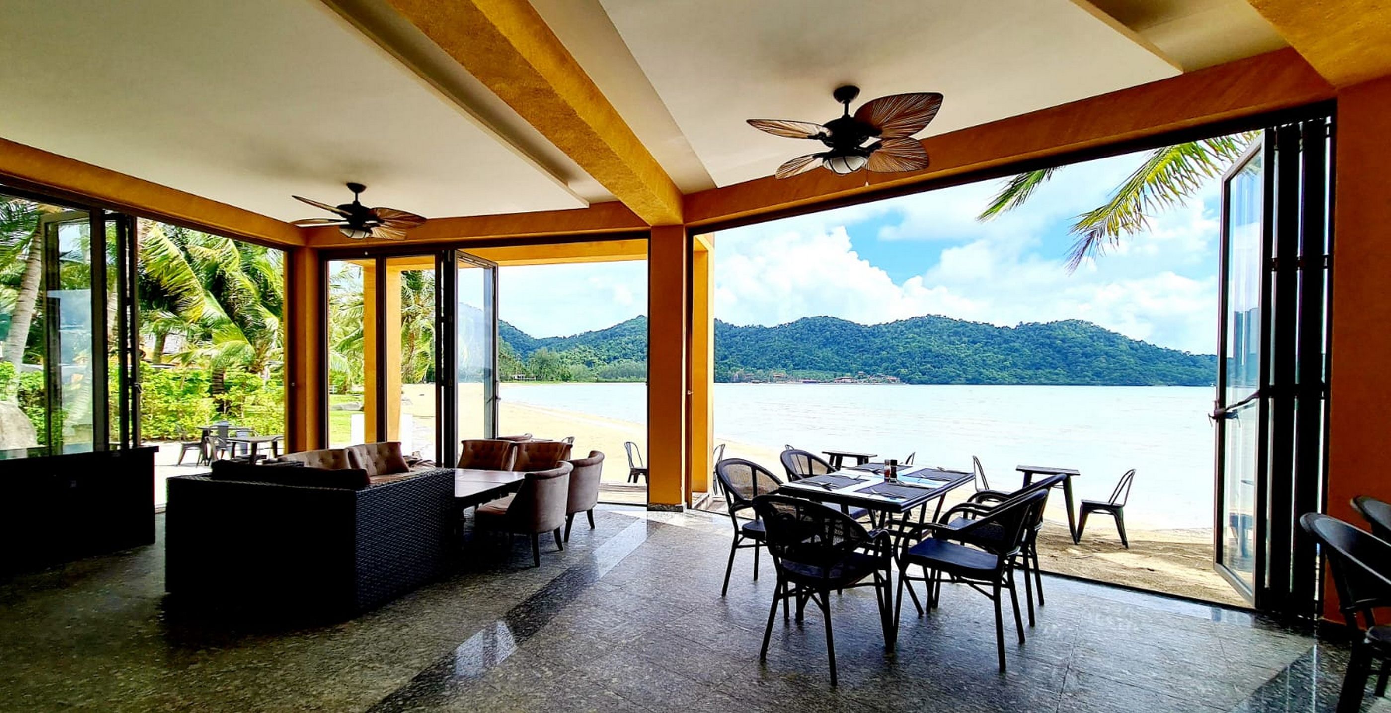 An open-plan dining area with a view of a lake and mountains, furnished with tables and chairs.