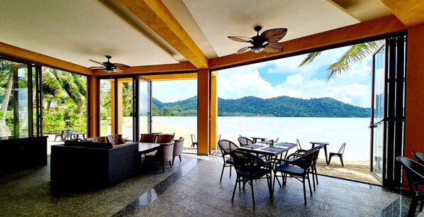 An open-plan dining area with a view of a lake and mountains, furnished with tables and chairs.