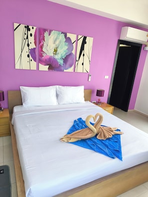 A hotel room with a large bed, a wall-mounted air conditioner, and a painting above the bed.