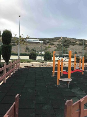 An outdoor exercise area with a metal fence, exercise equipment, and a paved surface. - Luxurious 2-Bedroom Apartment in Luz, Portugal (Luz)