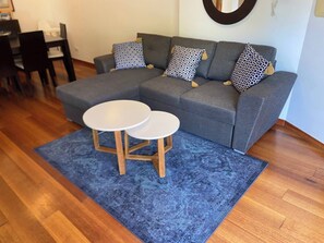 A living room with a grey sectional sofa, two round white tables, and a blue patterned rug. - Luxurious 2-Bedroom Apartment in Luz, Portugal (Luz)