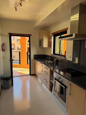 A modern kitchen with stainless steel appliances, a black countertop, and wooden cabinets. - Luxurious 2-Bedroom Apartment in Luz, Portugal (Luz)