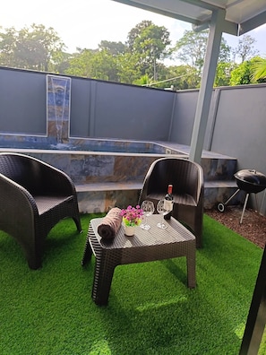 An outdoor patio with wicker furniture, a small table with a bottle and glasses, and a water feature in the background. - Villa Alomía, Private Pool,  10 People (Cahuita)