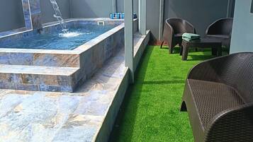A spa area with a hot tub, artificial grass, wicker furniture, and a water feature.