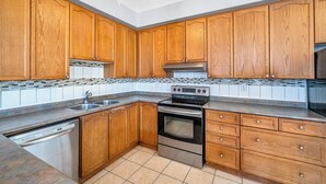 Een keuken met houten kasten, een roestvrijstalen vaatwasser, een dubbele oven en een betegelde spatwand.