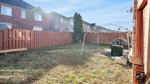 Een achtertuin met een houten omheining, een grote boom en een barbecue.