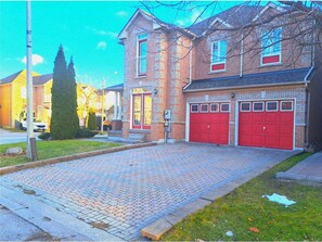 A residential building with a paved driveway, two red garage doors, and a brick facade. - King Bed, Home Gym, 4 TVs, Near Recreational Parks, Tennis Court, Shops! (Ajax)