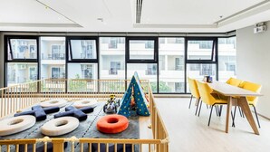 A modern room with large windows, a play area with cushions and a tent, and a dining area with yellow chairs. - Sea View 2 Bed Room Excellent Location (Muang Pattaya)