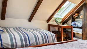 Un dormitorio con techo inclinado, una cama con ropa de cama a rayas, una pequeña mesa de madera y un estante con ropa doblada.
