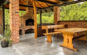 Eine Terrasse im Freien mit Kamin aus Ziegelsteinen, Holzbanken und einem Tisch.