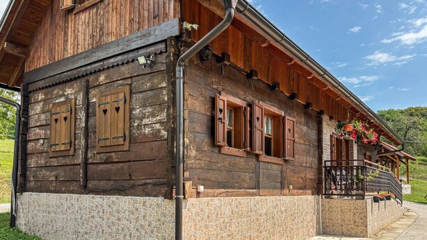 Una casa de madera con cimientos de piedra, varias ventanas con diseños de corazones y un balcón con plantas en macetas.