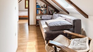 Un dormitorio tipo loft acogedor, con techo inclinado, estantería empotrada, sofá cómodo y banco de madera.